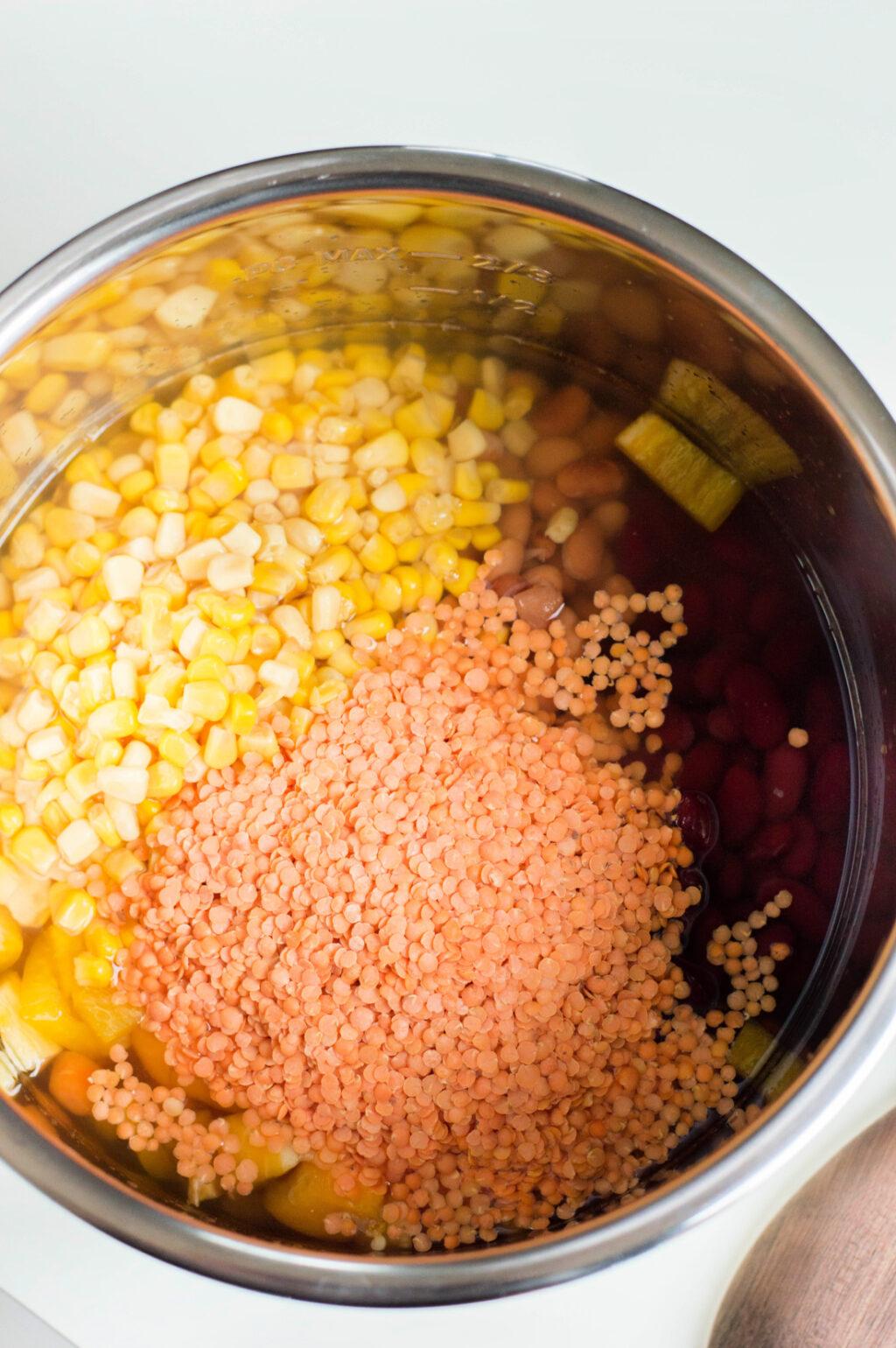A cooking pot filled with vegetarian instant pot chili, featuring layers of red beans, orange lentils, and yellow corn on a stove.
