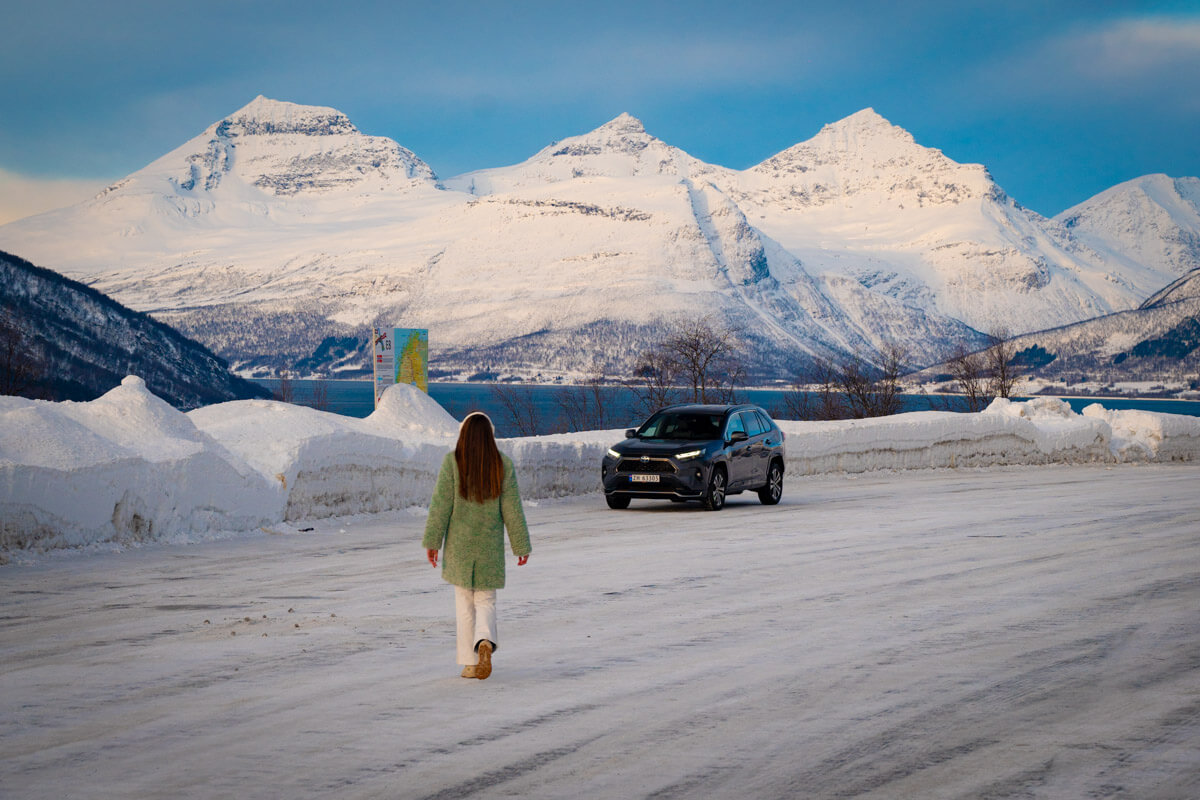 walking tornados a rental car in Tromso, Norway, surrounded by snow and mountains