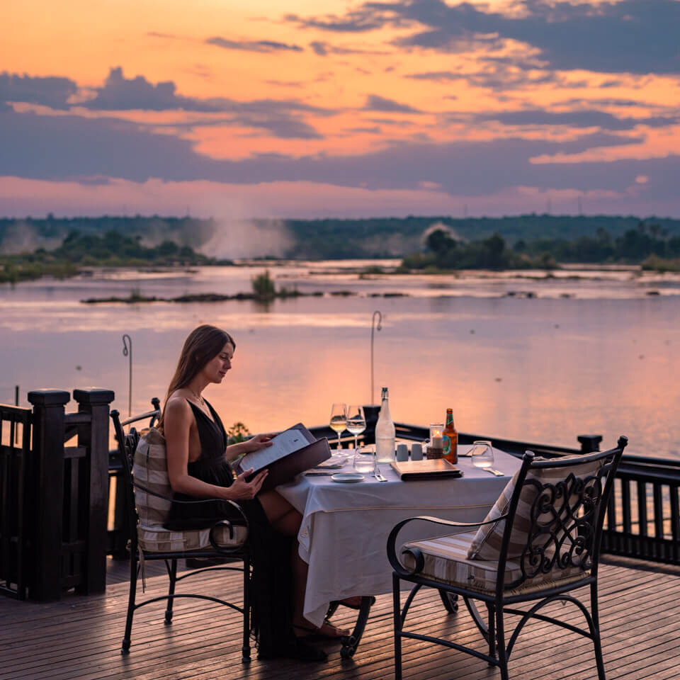 girl with dress sitting at the dinner table next to the Zambezi river during sunset at the Royal Livingstone Hotel in Zambia
