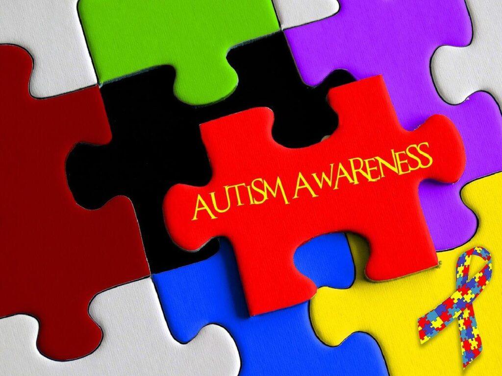 Interlocking puzzle pieces in red, green, blue, and purple, featuring the words "understand autism" and a ribbon with puzzle pattern.