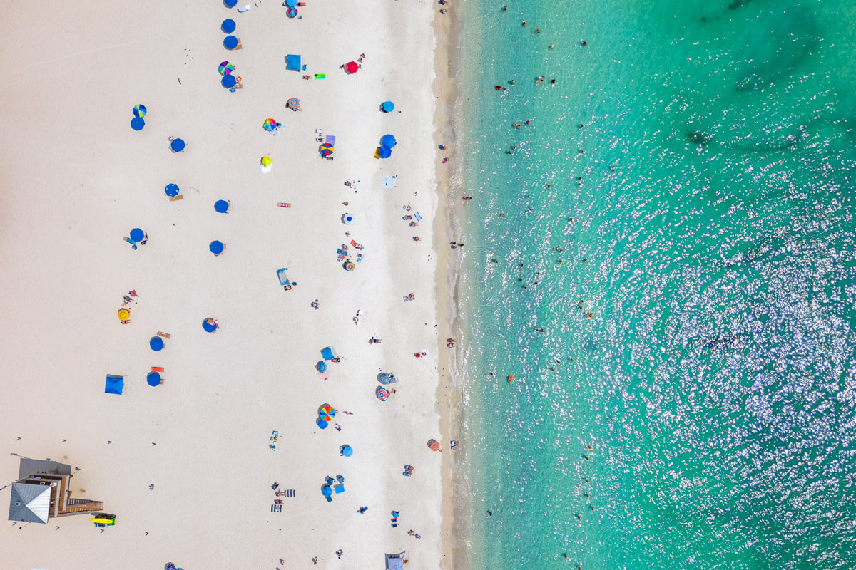 drone view of sandy beach with parasols and blue ocean on Anna Maria Island, Florida